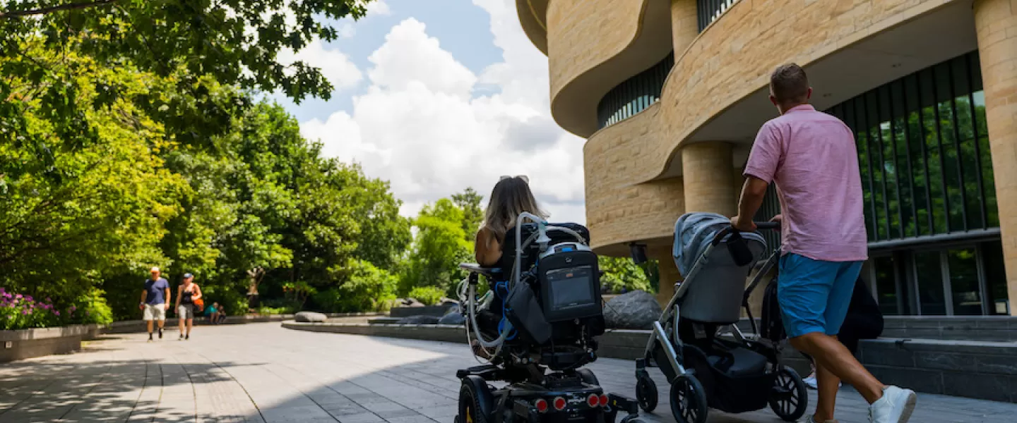 A family outside a museum, one pushing a stroller and another in a wheelchair
