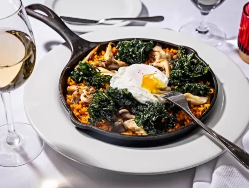 skillet with paella, kale and fresh egg on a white table spread