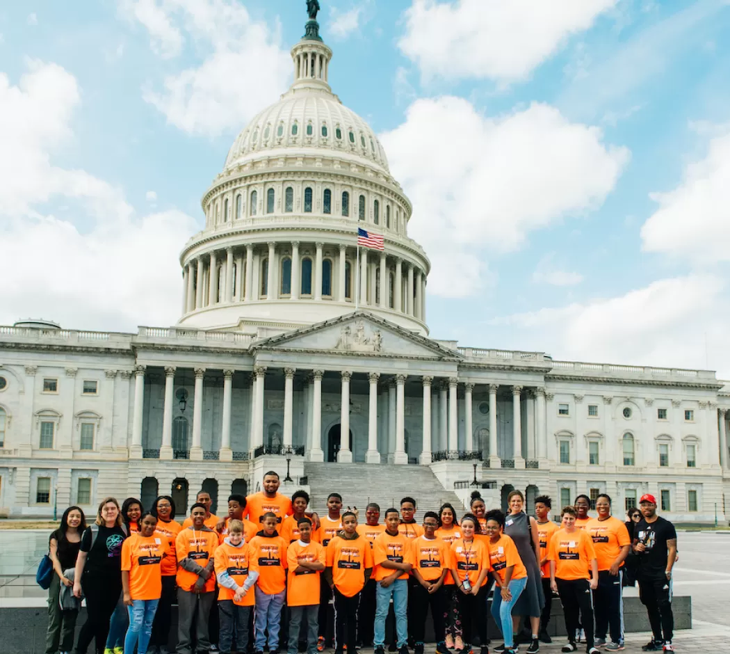 A large group of students are gathered in front of the US Capitol on a field trip.